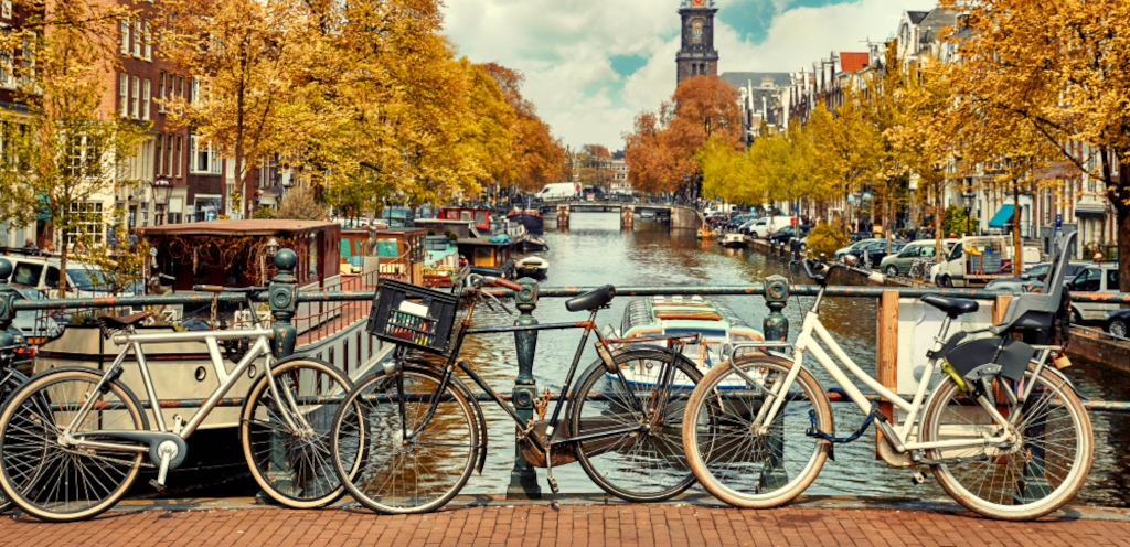 Vier fietsen geparkeerd op een brugleuning langs een gracht in Amsterdam met herfstkleurige bomen en historische gebouwen voor de Werelfietsdag 2025.